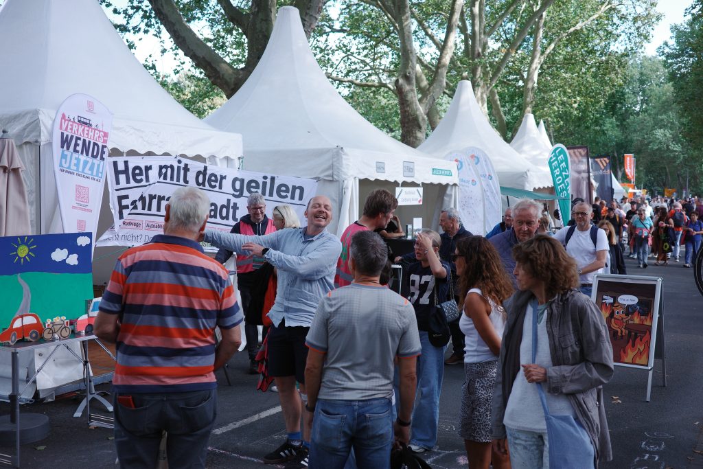 Eine Menschenmenge vor verschiedenen Aktions- und Infoständen auf der Meile, darunter Hinweisschilder und Plakate.