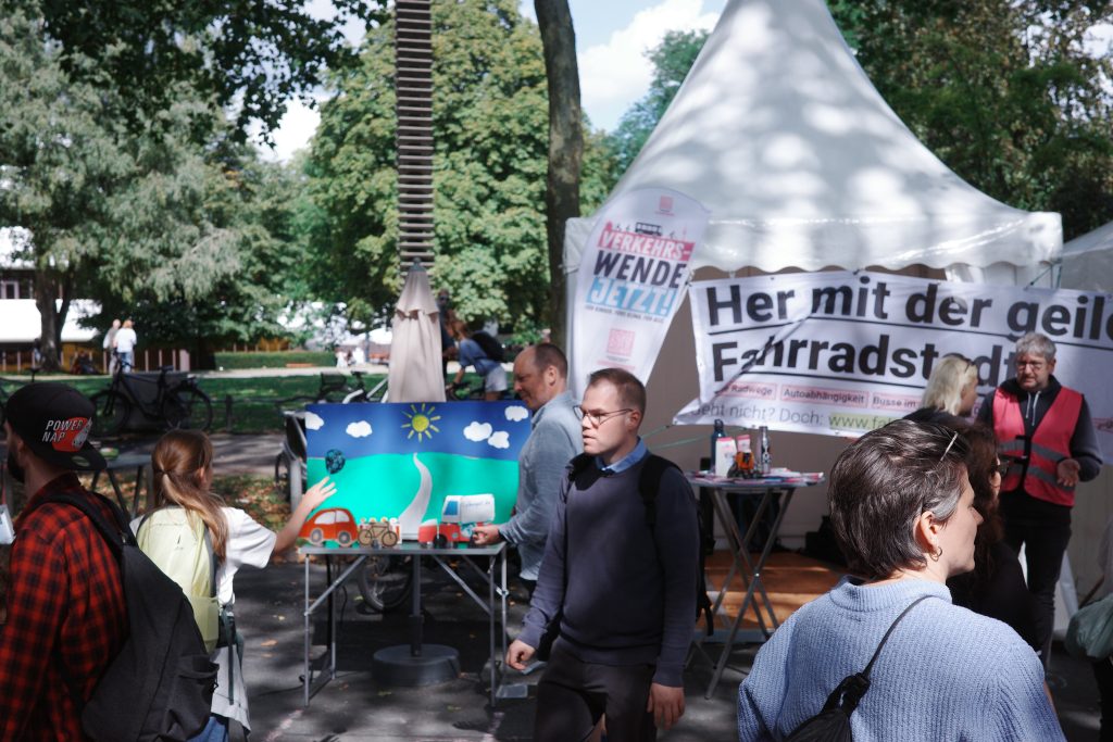 Ausschnittaufnahme des Standes mit Infomaterial, Dosenwerfen, Flyern und dem Banner „Her mit der geilen Fahrradstadt“.