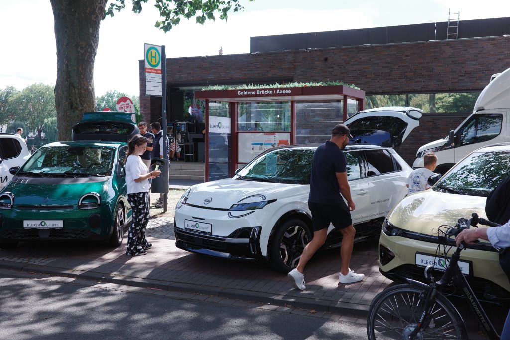 Mehrere auf dem Gehweg und an einer Bushaltestelle geparkte E-Autos, umgeben von Fußgängern.
