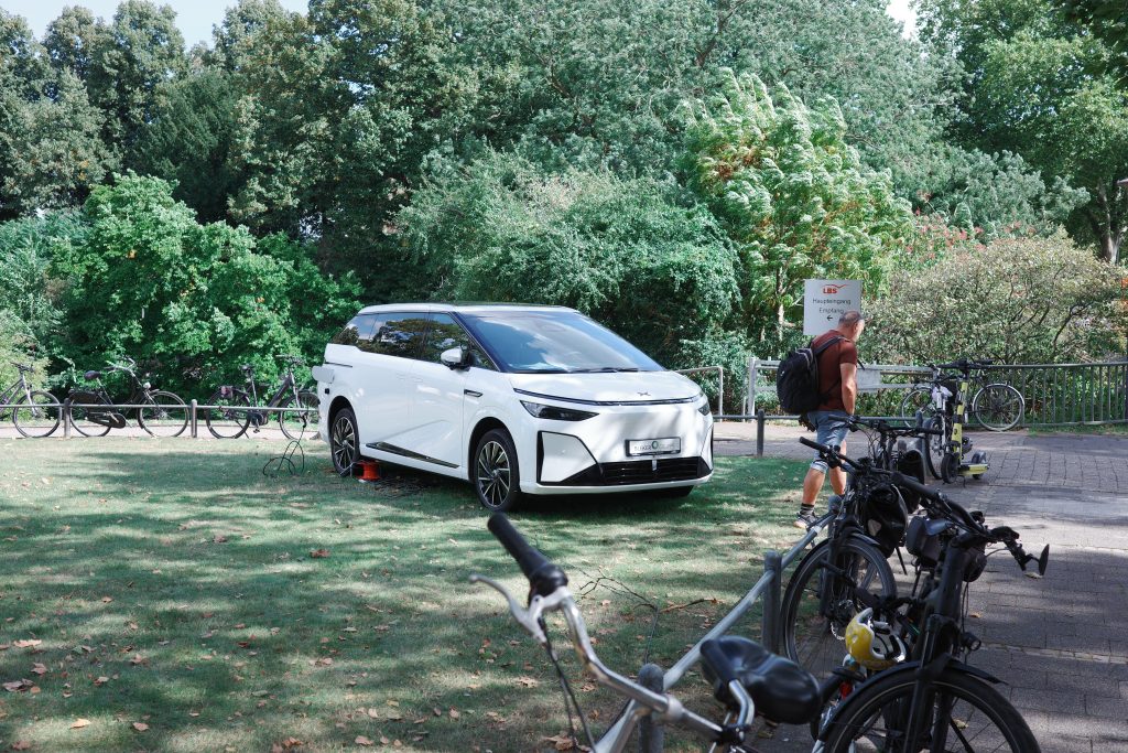 Ein weißes Elektroauto steht auf einer Rasenfläche direkt neben Fahrradständern.